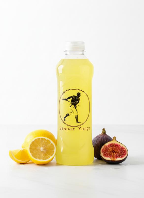 Bouteille de sport Yanga remplie d'une boisson jaune, entourée de tranches de citron et d'une figue fraîche sur fond blanc lumineux